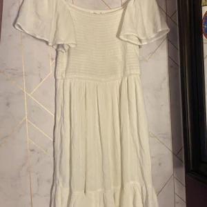 Vit offshoulder klänning KappAhl 164 - Superfin vit klänning från KappAhl i storlek 164. Offshoulder-modell med vida, korta ärmar och smock upptill. Kjolen är luftig och har volangkant nertill. Perfekt för sommarens varma dagar och har en lätt, flowy känsla. Den passar mig som har S/xs i storlek. Den är inte genomskinlig då den har vit lager tyg undertill.