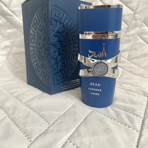 Lattafa Asad Zanzibar parfym 100ml - Lattafa Asad Zanzibar Eau de Parfum i en snygg blå flaska med silverdetaljer och orientaliskt mönster. Flaskan rymmer 100 ml och har en modern, stilren design med arabiska inslag. Kommer i matchande blå kartong med lejonmotiv och silvertryck. Använd typ 10 gånger och boxen följer med.