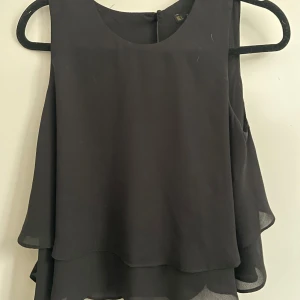 Svart ärmlös blus med lager från Zara - Svart blus i luftig modell med dubbla lager och rund halsringning från Zara. Ärmlös design som ger en stilren och enkel look. Perfekt att matcha med jeans eller kjol för en clean vibe.