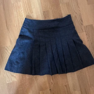 Mörkgrå kortkjol - Snygg mörkgrå plisserad kortkjol med bred linning och klassisk skoluniformsvibe. Kjolen har en stilren look och passar perfekt till en stickad tröja eller oversized hoodie.