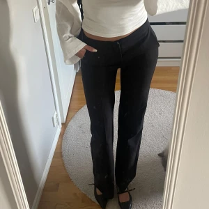 Svarta kostymbyxor med wide fit - Snygga svarta kostymbyxor med hög midja och raka, vida ben. Byxorna har klassisk passform och stängs med dragkedja och knapp framtill. Perfekta för en clean och stilren look.