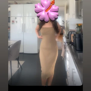 Beige ribbad långklänning - Säljer en beige ribbad långklänning med tight passform och ärmlös design. Klänningen har en rak, kroppsnära siluett och är perfekt för dig som gillar en stilren look. Materialet är stickat och stretchigt vilket gör den superbekväm. Med prislapp