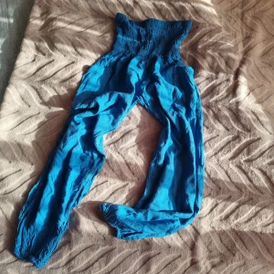 Haremsbyxor för barn - Superskön blå haremsbyxa med smockad överdel och långa, vida ben. Perfekt för varma dagar och enkel att styla med sneakers eller sandaler. Tunt och luftigt tyg som känns riktigt bekvämt. De har en ficka i varje sida. Dom är inköpta i Thailand åt ett barn på 4-6 år, men dom kan nog passa äldre än så, ingen lapp med storlek finns Aldrig använda.