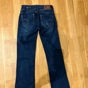 G-Star RAW Midge Bootcut jeans blå - Snygga mörkblå jeans från G-Star RAW, modell Midge Bootcut. Klassisk femficksdesign, kontrastsömmar och läderpatch bak i midjan. Jeansen har bootcut-ben och är tillverkade i slitstarkt denimtyg. Perfekta för dig som gillar en tidlös och cool look.