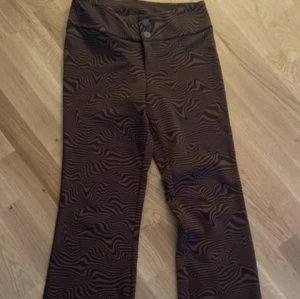 Bruna zebra-mönstrade bootcut byxor - Snygga bruna byxor med zebramönster och bootcut-snitt. Byxorna har hög midja och stängs med två knappar framtill. Perfekta för dig som vill sticka ut med ett coolt mönster och trendig passform.