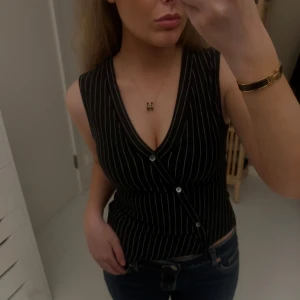 Svart randig omlott-linnetopp - Säljer en svart ärmlös linne-topp med vita tunna ränder och omlottknäppning framtill. Djup v-ringning och smickrande passform som framhäver midjan. Perfekt att styla med jeans eller kjol för en cool look. Använd en gång!❤️