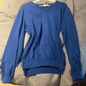 Blå v-ringad tröja från Boomerang - Blå v-ringad tröja från Boomerang med liten broderad logga på bröstet. Tröjan har långa ärmar, ribbade muddar och är i mjuk bomull. Perfekt för lager-på-lager och chill vibes. Passar alla storlekar skulle jag säga