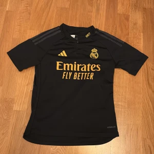 Real Madrid svart guld fotbolls set med tröja shorts och strumpor 152  - Säljer en svart Real Madrid fotbollströja från Adidas som jag köpte i spanien i realmadrid egna butik med guldiga detaljer och klubbmärke på bröstet. Tröjan har korta ärmar och är tillverkad i ett lätt och ventilerande material. Perfekt för dig som vill ha en snygg tröja att ha på träningen eller match. Skriv om du enbart vill ha ett plagg separat 