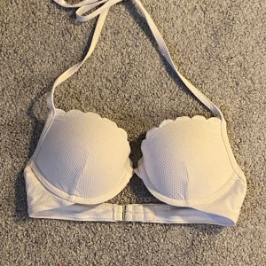 Vit bikiniöverdel med  från H&M!  - Supersöt vit bikiniöverdel från H&M med vadderade kupor. Bikinin har knyt i nacken och klassisk knäppning bak. Materialet är lätt strukturerat och ger en fräsch känsla till sommarens strandhäng.Absoluta nyskick!  Inga skador eller anmärkningar  Knappt använd   Storlek 70B