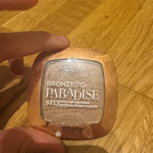 L'Oréal Bronze to Paradise bronzer - Bronzer i nyansen 03 Back to Bronze från L'Oréal Paris. Kommer i en snygg fyrkantig ask med roséguldfärgat lock och palmbladsmönster i pudret. Ger en naturlig solkysst look och innehåller 84% ingredienser av naturligt ursprung. Är Max använd 2 gånger va inte min färg 