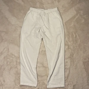 Vita linnebyxor med snörning - Snygga vita linnebyxor med elastisk midja och snörning. Byxorna har raka ben och en avslappnad passform, perfekta för varma dagar. Fickor på sidorna och en bakficka ger en chill vibe. Lätta och luftiga i materialet.