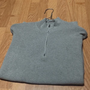 Grå stickad half zip från Polo Ralph Lauren - Snygg grå stickad tröja från Polo Ralph Lauren med half zip och diskret broderad logga på bröstet. Tröjan har lång ärm, ribbade muddar och en klassisk ståkrage. Perfekt för lager-på-lager och chill höst- eller vinterstil.