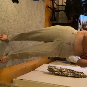 Beiga kostymbyxor med rak passform - Snygga beiga kostymbyxor med hög midja och raka ben. Byxorna har klassisk design med pressveck och bälteshällor. Perfekta att styla med en crop top eller oversized skjorta för en clean look.