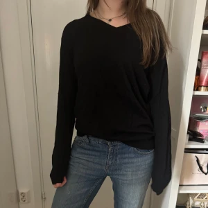 Svart cashmere tröja med döskallemönster - Svart långärmad cashmere tröja med v-ringning och stort döskallemönster i vitt och rött på ryggen. Detaljer med samma mönster på ärmarna. Perfekt för dig som vill sticka ut med en cool och edgy stil.