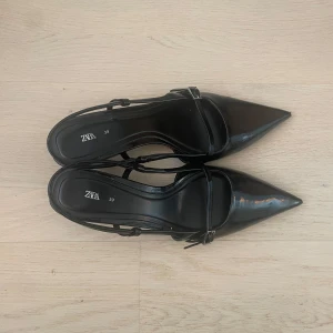 Svarta kitten heels från Zara - Svarta klackskor från Zara med smala remmar och spetsig tå. Skorna har en elegant klack och en snygg spänndetalj vid sidan 😍. Perfekta för dig som gillar stilrena och trendiga skor. Supersnygga till ett par jeans eller fin klänning för att piffa till din outfit💕De har små slitmärken på klacken och under (se sista bild)
