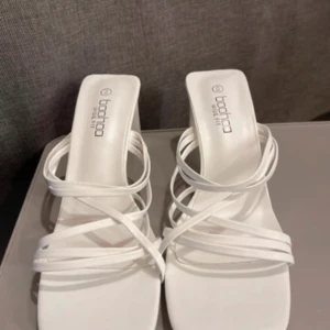 vita klackar från Boohoo - Säljer ett par stilrena vita klackar från Boohoo med smala remmar och fyrkantig tå. Skorna har en medelhög klack och öppen tå, perfekta för sommarens alla tillfällen.