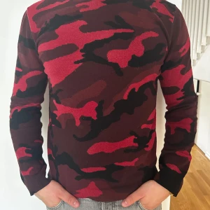 Valentino tröja (bytes tas) - Säljer en långärmad tröja med röd och svart camouflagemönster på framsidan och ärmarna. Baksidan är helsvart med nit. Tröjan har en normal passform och är tillverkad i ett mjukt material, perfekt för dig som vill sticka ut. Märke valentino. Modellen är 183 cm lång.