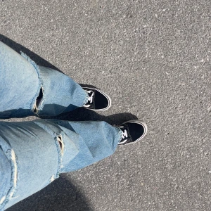 Blå slitna jeans med vida ben - Säljer ett par blå jeans med vida ben och slitna detaljer vid knäna. Jeansen har en avslappnad passform och är perfekta för en cool och trendig stil. Passar dig som gillar streetwear och vill ha ett par statement-jeans.