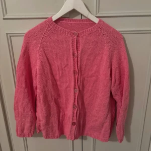 Rosa stickad kofta - Säljer en söt rosa stickad kofta med rund halsringning och knäppning framtill. Koftan har långa ärmar och är perfekt för lager-på-lager. Enkel och stilren design som passar till mycket.