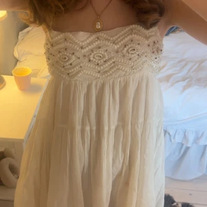 Vit klänning med pärldetaljer - Superfin vit axelbandslös klänning med broderade pärlor och paljetter upptill. Klänningen har en flowy passform och är perfekt för sommarens alla tillfällen. Materialet känns lätt och luftigt. 
