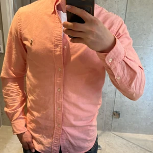 Ralph Lauren Skjorta - Säljer denna snygga Ralph Lauren skjorta i en väldigt snygg Rosa/Coral färg. Skjortan är i storlek S men kan passa Xs också. Skjortan är i skönt material toppen nu till sommaren. Skriv vid funderingar.