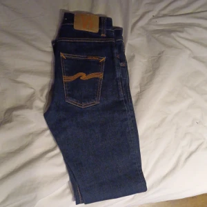 Nudie Jeans lean Dean mörkblå - Säljer ett par klassiska mörkblå jeans från Nudie Jeans med raka ben och snygga kontrastsömmar. Byxorna har fem fickor och Nudie-loggan broderad på bakfickorna. Perfekta för dig som gillar stilrena och tidlösa jeans. I storlek W28 L32 i modellen Lean dean dem är helt nya men prislapp  och sånt ha jag råka kasta jag är prutbar vid snabbaffär skriv om du har några frågor eller funderingar 