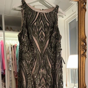 Klänning från Adrianna Papell - Säljer en superfin svart glittrig klänning från Adrianna Papell med geometriskt mönster och paljetter. Klänningen är ärmlös och har en snygg hög form vid halsen. Perfekt för dig som vill sticka ut på festen! Klänningen är ny och oanvänd! 