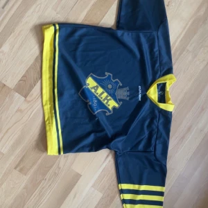 AIK hockeytröja från Bauer - Säljer en blå och gul AIK hockeytröja från Bauer i storlek 130/140. Tröjan har AIK-logga på bröstet, gula detaljer vid ärmslut, hals och nederkant samt två gula ränder på ärmarna. Tillverkad i 100% polyester.