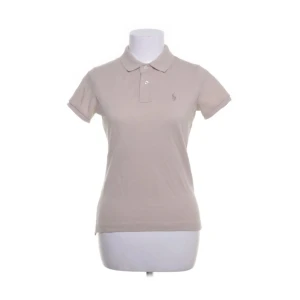 Beige pikétröja från Ralph Lauren - Säljer en beige pikétröja från Ralph Lauren, modell The Skinny Polo. Tröjan har korta ärmar, klassisk krage och knäppning framtill. Tillverkad i 100% bomull och har en liten broderad logga på bröstet.