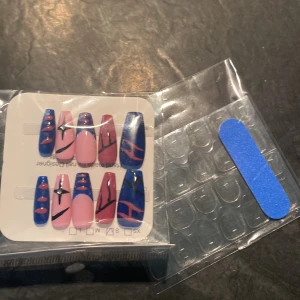 Färgglada lösnaglar med blå och rosa design - Säljer ett set lösnaglar i olika storlekar med coolt blått och rosa mönster, vissa med svarta linjer och dekorstenar. Medföljer självhäftande klisterlappar och en blå nagelfil. Perfekt för att fixa snygga naglar snabbt.