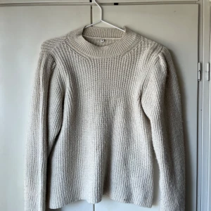 Beige stickad tröja med små puffarm  - Mysig beige stickad tröja med rund hals och små puffärm. Tröjan har en enkel och stilren design med ribbade mönster,Perfekt för kyliga dagar. Har ändas använts 1-2 gånger