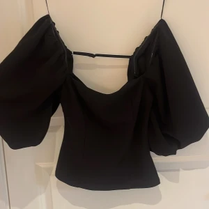 Svart topp med puffärmar från BikBok - Trendig svart topp från BikBok med stora puffärmar och fyrkantig ringning. Toppen har en croppad passform och är perfekt för att skapa en statement-look. Tillverkad i ett mjukt material som sitter snyggt på kroppen.