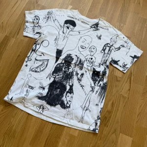 Vit t-shirt med svart grafiskt tryck från Fucking Awesome size L  - Säljer en vit t-shirt från Fucking Awesome i storlek large med unikt svart grafiskt tryck över hela plagget. T-shirten har korta ärmar och en klassisk passform. Perfekt för dig som gillar streetwear och vill sticka ut med en kreativ design.