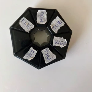 Svart medicinask med fack för veckodagar - Säljer en svart, sexkantig medicinask med separata fack för varje veckodag. Perfekt för att organisera tabletter eller småsaker. Locket är genomskinligt och varje fack är märkt med veckodag på engelska. Praktisk och smidig att ha med sig.