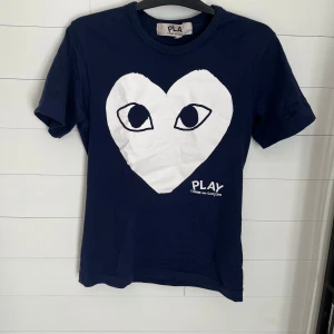 Blå t-shirt från Comme des Garçons Play - Mörkblå t-shirt från Comme des Garçons Play med stort vitt hjärta och ögon på bröstet samt PLAY-tryck. Perfekt nu till sommaren.|Skriv vid intresse eller fler bilder😊|