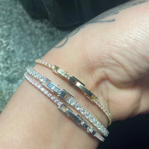 Tennisarmband i guld och silver med stenar - Säljer flera stilrena tennisarmband i både guld- och silverfärg, dekorerade med gnistrande stenar. Perfekta att bära tillsammans eller var för sig för en lyxig känsla. Armbanden har klassiska länkar och smidig låsning.