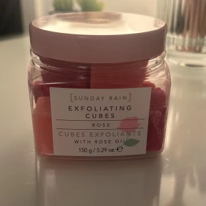 Exfoliating Cubes Rose från Sunday Rain - Burk med exfolierande kuber i rosa nyanser, doft av ros och berikade med rosolja. Perfekta för att skrubba huden mjuk och fräsch. Innehåller 150 g. Aldrig använda. 