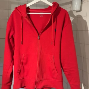 Polo ralph lauren zip - Röd zip-hoodie från Ralph Lauren Supersnygg och klassisk hoodie i rött från Ralph Lauren. Mjuk och skön i materialet, perfekt att slänga på sig till vardags eller som layering under en jacka. Dragkedja framtill, huva med snören och två fickor. Ikoniska lilla Polo-loggan broderad på bröstet.  Använd men i fint skick, inga fläckar eller hål. Priset går att diskutera. Är bara att skriva om ni har några funderingar👍
