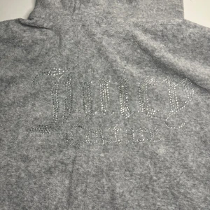 Grå hoodie med strass från Juicy Couture - Grå hoodie från Juicy Couture med glittrande strassdetaljer på ryggen och bröstet. Klassisk dragkedja framtill och mjukt material som känns lyxigt. Säljer för att den är för liten, priset kan diskuteras💗🩷💓💕