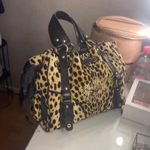 Vintage daydreamer från juicy couture  - Juicy Couture handväska i leopardmönster med svarta detaljer och stor svart rosett på sidan. Väskan har broderad logga på framsidan Insidan är fodrad med tryckt Juicy Couture-mönster. Går inte att få tag på längre därav priset. Kom gärna med bud! Kommer inte lägga mig under 1200kr.