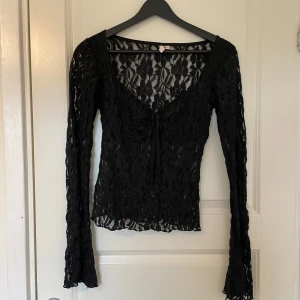 Svart spetsblus från Nelly - Säljer en svart långärmad spetsblus från Nelly. Blusen har v-ringning, knyt framtill och är helt genombruten i spetsmaterial. 