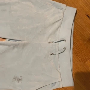 Ljusblå velourbyxor från Juicy Couture - Limited edition Ljusblåa mjukisbyxor i velour från Juicy Couture. Byxorna har strassdetaljer med Juicy Couture-logga på ena benet och bak. 