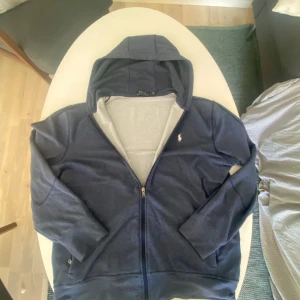 Blå hoodie från Polo Ralph Lauren - Mörkblå zip hoodie i perfekt skick. Nästan aldrig användas och kostar 1400 ny. Lite liten i storleken passar M bra