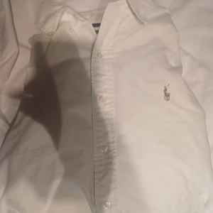 Vit skjorta från Ralph Lauren - Klassisk vit skjorta från Ralph Lauren med broderad logga på bröstet. Skjortan har knappar framtill och en stilren krage. Perfekt för dig som gillar en tidlös och clean look. Son är typ I helt ny skick köpte den men sen var den fär stor för mig de är i XL jag är prutbar vid snabbaffär skriv om du har några frågor eller funderingar 