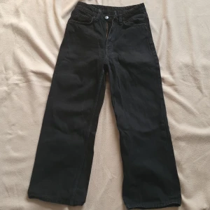 Svarta vida jeansbyxor - Säljer ett par svarta jeansbyxor med breda ben och klassisk femficksdesign. Byxorna har hög midja och stängs med dragkedja och knapp. Liten dragen tråd på baksida vänster ben (se bild 5) men syns knappt. Därav priset 