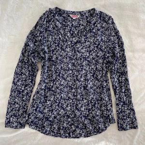 Blå långärmad skjorta med blommor från Indiska - Marinblå skjorta med ett blommigt mönster i vitt, mjukt luftigt material, svarta knappar på framsidan