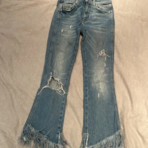Blå jeans med fransar från Zara - Trendiga blå jeans från Zara med fransar ner till benslutet och en kortare modell som slutar ca 3 cm ovanför ankeln är en riktigt snygg och modern detalj. Den korta längden gör att du kan visa upp dina skor på ett bra sätt, och fransarna ger en lekfull och unik touch. Perfekt för att skapa en avslappnad men ändå stilmedveten look!