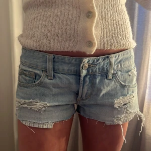 Ljusblå slitna jeansshorts från Abercrombie & Fitch - Säljer ett par ljusblå jeansshorts från Abercrombie & Fitch med slitna detaljer och råa kanter. Klassisk femficksmodell med låg midja och knappgylf. Perfekta för sommaren! INTRESEKOLL 