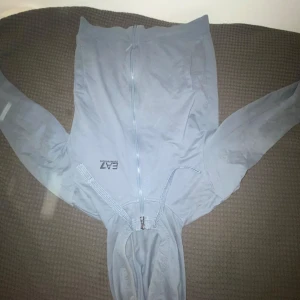 Ljusblå hoodie från EA7 Emporio Armani - Säljer en ljusblå hoodie från EA7 Emporio Armani med dragkedja och huva. Jackan har snörning vid huvan och logga på bröstet. Perfekt för en avslappnad stil.