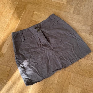 Olivgrön kortkjol - Olivgrön kjol med två knappar framtill, bälteshällor och en enkel, rak passform. 